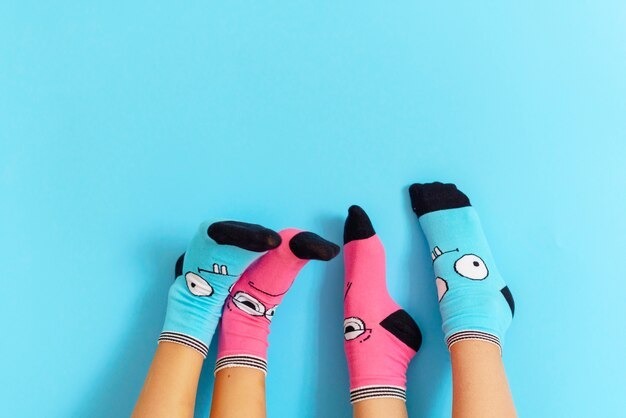 Two pairs of feet raised against a light blue background, wearing mismatched funny cartoon socks in bright pink and blue colors.