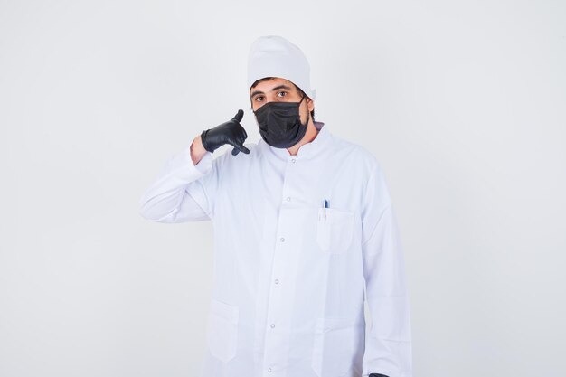 A male doctor or chef wearing a white gown, cap, black face mask, and gloves, making a "call me" hand gesture.