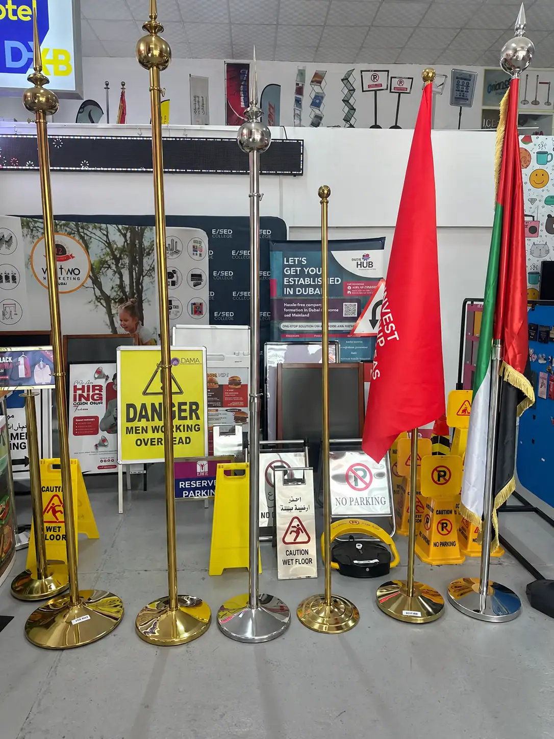 Showroom display of brass and stainless steel flag poles, indoor UAE flag stands, and safety signboards for Customized Corporate Gifts Dubai and Promotional Gifts.